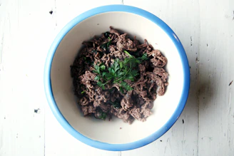 Raw ground beef in a rustic bowl with fresh herbs around.