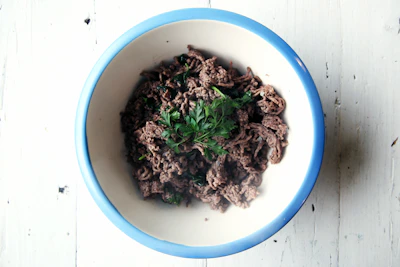 Raw ground beef in a rustic bowl with fresh herbs around.