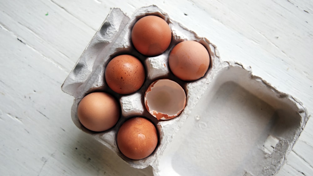 Cinco huevos enteros y un huevo medio abierto dentro de una bandeja de huevos abierta