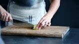 person slicing green vegetable on chopping board