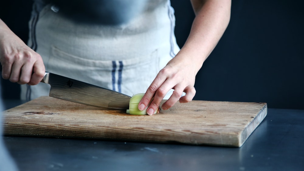 personne coupant un légume vert sur une planche à découper