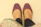 Hand holding a pair of royal blue and red embroidered juttis against a black background with gold accents
