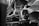 A boxer sits in focus with his mouth slightly open, while a team member wearing gloves tends to his face during a break in a boxing match. The scene is intense and dynamic, captured in black and white, with out-of-focus shadows framing the central figure.