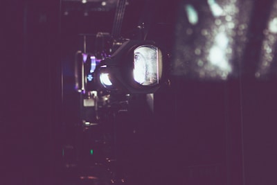 A close-up view of a vintage film projector with a focused lens. The scene is dimly lit with soft light emanating from the projector, creating a nostalgic and cinematic atmosphere.