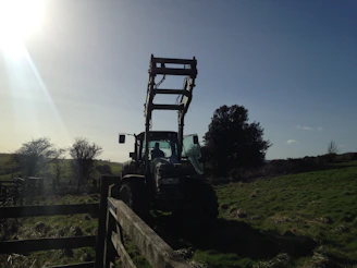 Two brothers standing beside a tractor with a pile of cleared junk in a sunny yard.