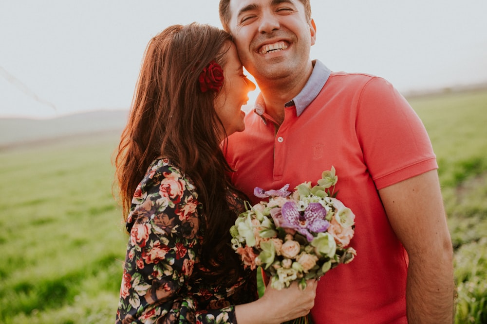 A man and a woman laughing in a sunny field. She holds a bouquet of flowers.