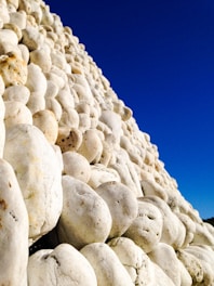 A collection of smooth, white stones stacked closely together, forming a textured surface. The sky in the background is clear and bright blue, providing a stark contrast to the stones.