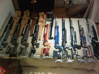 Close-up of decorated plastic gun stocks lined up on a rustic wooden bench, highlighting hydrographic patterns.