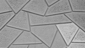 A textured surface composed of various geometric shapes, predominantly triangles and quadrilaterals, arranged in a mosaic-like pattern. The rough texture of the material gives a tactile appearance, while the shapes fit together with clean edges and borders.