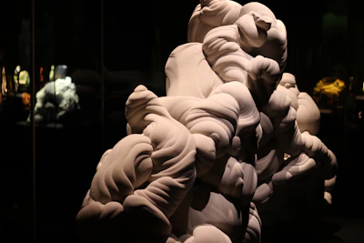 An abstract sculpture made of smooth, flowing wood shapes displayed on a minimalist pedestal.
