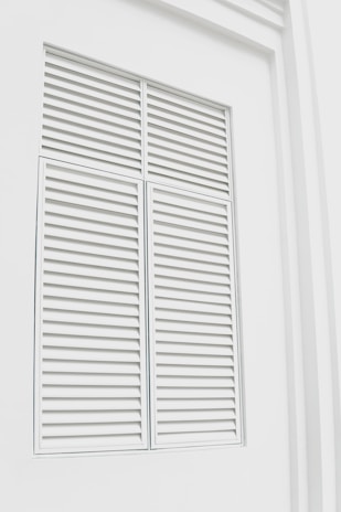 Close-up of elegant white plantation shutters perfectly fitted on a sunlit living room window.