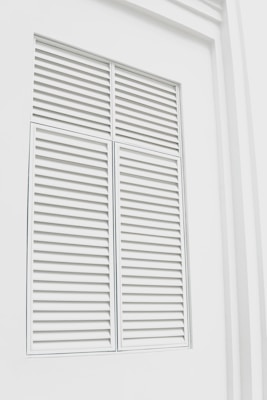 White louvered shutters set in a wall, with a clean, minimalist design. The shutters have horizontal slats that are evenly spaced.