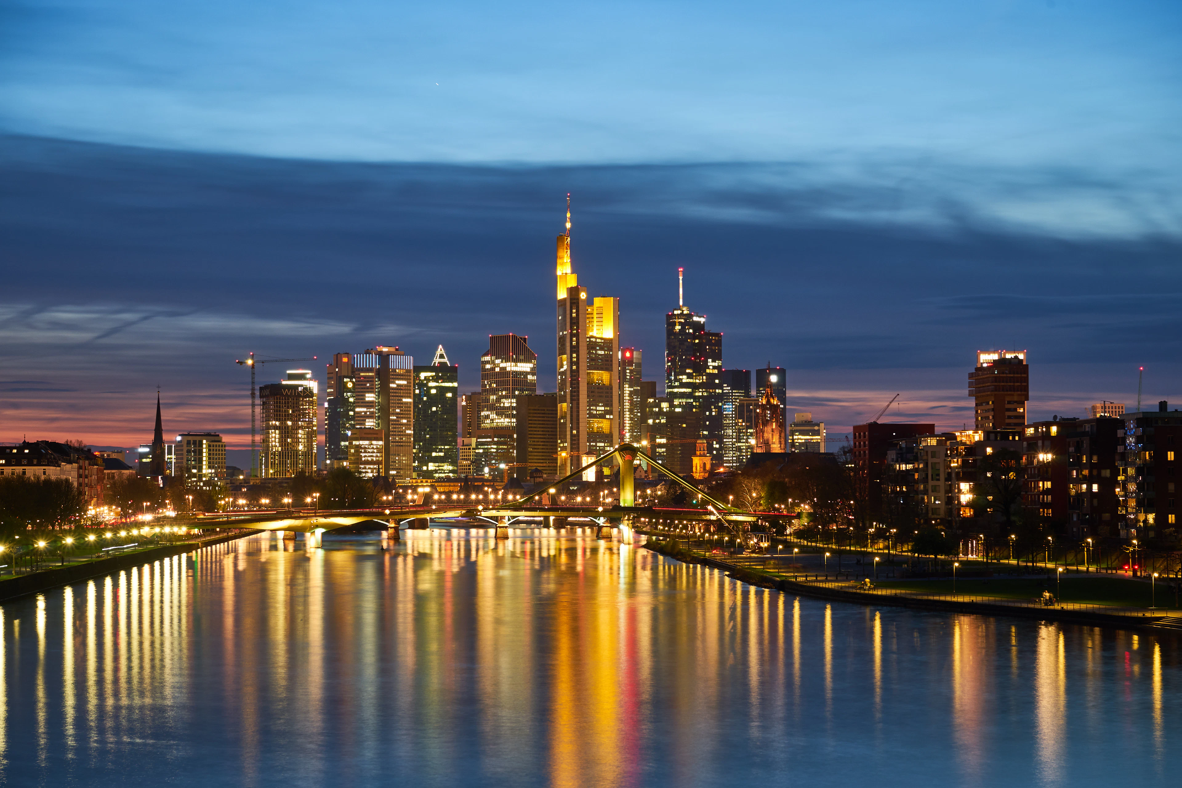 Frankfurt's banking towers lit at dusk above the Main, their reflections running down the river