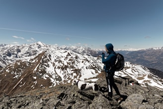 A traveler wearing a thick jacket standing on a mountain peak overlooking a valley