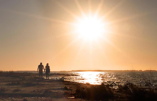 A candid shot of a couple walking hand in hand along a sun-drenched beach at golden hour.