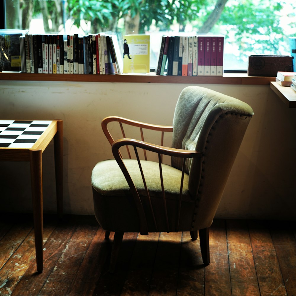 An armchair, checkered table, and books in a room with wooden floorboards