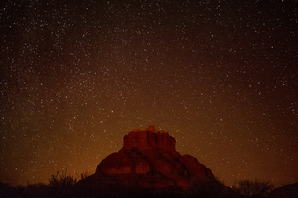 Brauner Berg unter dem Sternenhimmel während der Nacht in der Zeitrafferfotografie