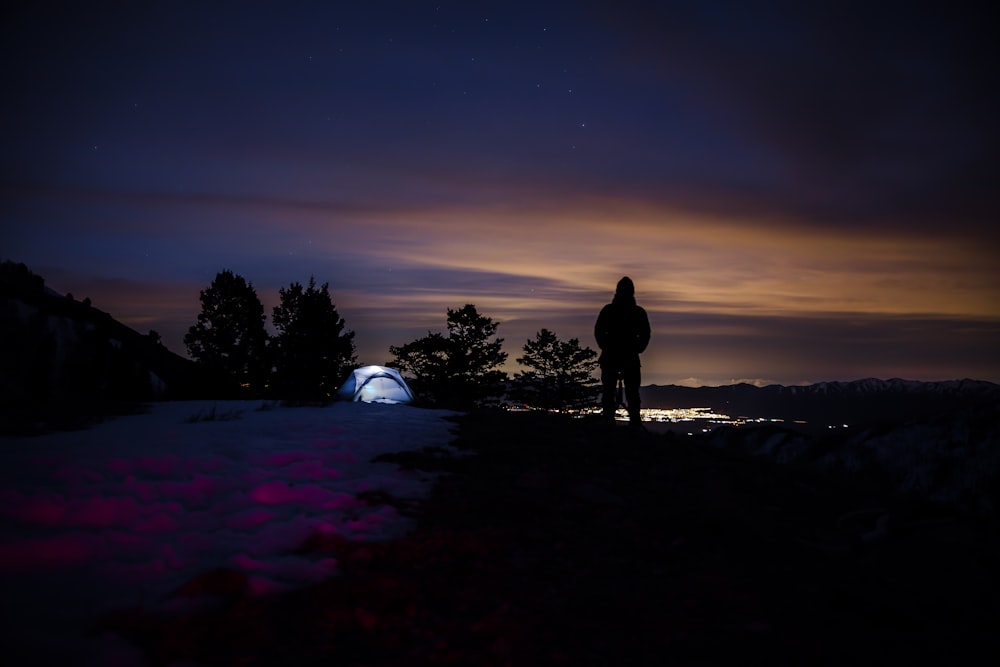 silhouette of hooded person with tent in background