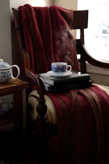 A sunlit reading nook with a plush armchair, soft throw blanket, and a small wooden side table holding a steaming cup of tea.