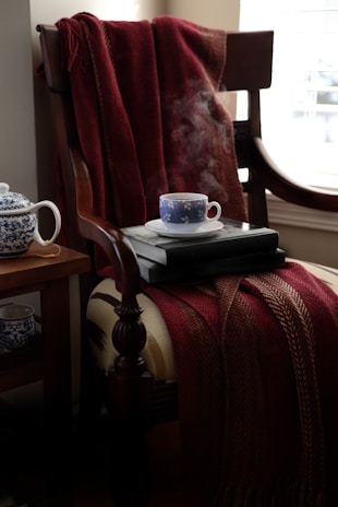 A plush armchair draped with a fluffy blanket next to a small side table holding a steaming cup of tea.