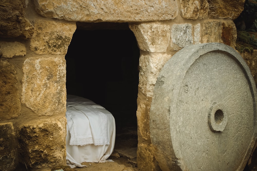 A cement wheel next to a brick building with a sheeted bed inside.