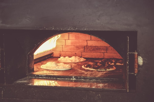 A commercial pizza oven in action, with chefs preparing multiple pizzas in a busy kitchen.