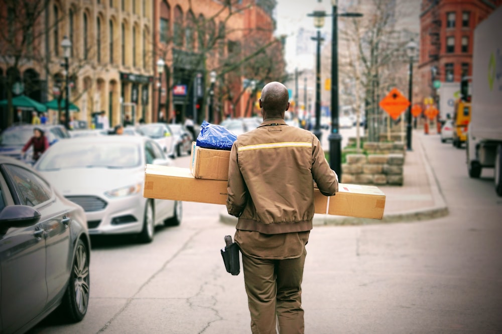 A bald man in uniform is carrying parcels next to a busy street in St. Lawrence Market.