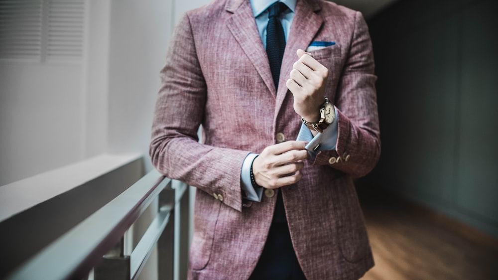 man in maroon suit jacket beside window with railings