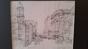 A sketchbook open to a finely detailed pencil drawing of a city street.