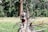 A person is walking along a fallen tree trunk in a lush green forested area. They are wearing a hat, a backpack, and athletic wear, and appear to be hiking or exploring the natural surroundings.