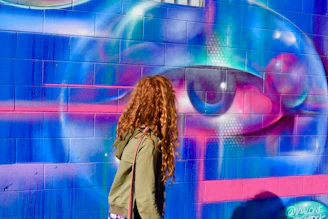 Woman with curly hair smiling against a colorful mural