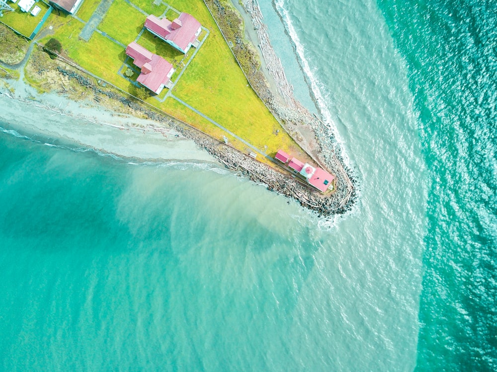 Photographie aérienne d’une maison rose au bord d’un terrain près d’un plan d’eau