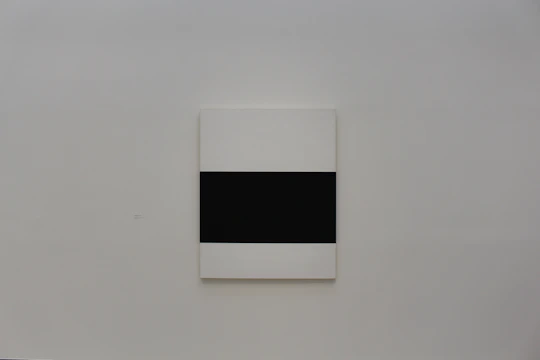 A minimalist framed artwork hanging on a dark wall, illuminated softly by ambient light.