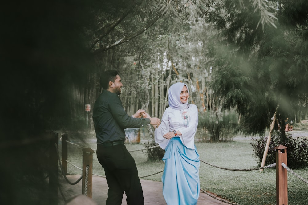 man smiling looking at woman smiling and standing on bridge near green leaf trees during daytime