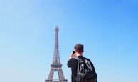 A traveler capturing a photo under the Eiffel Tower in Paris during a sunny afternoon.