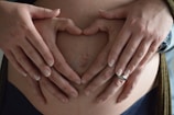 Close-up of hands forming a heart shape over a baby bump with soft natural light.