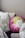 A collection of pillows arranged on a bed or couch. One pillow is round with a vibrant floral design in pink, green, and white colors. Other pillows feature black and white leaf patterns, while another has black and white stripes. The setting appears cozy and inviting.