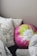 A collection of pillows arranged on a bed or couch. One pillow is round with a vibrant floral design in pink, green, and white colors. Other pillows feature black and white leaf patterns, while another has black and white stripes. The setting appears cozy and inviting.