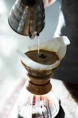 Barista carefully pouring hot water over coffee grounds in a glass Chemex brewer.