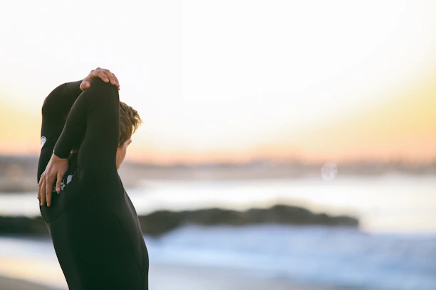 A smiling young woman in workout clothes stretching outdoors at sunrise.