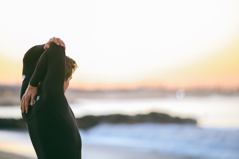 depth of field photography of person in black wetsuit standing in front of shore