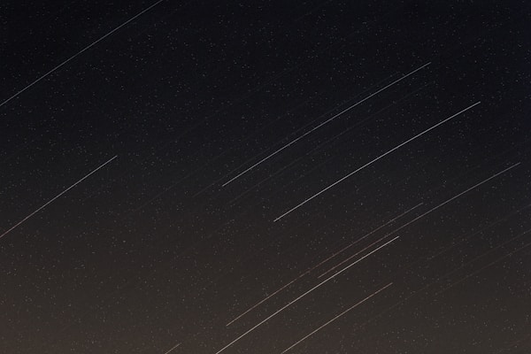 Long trails of light streak across a dark sky, indicating star trails caused by long-exposure photography, with faint stars visible in the backdrop.
