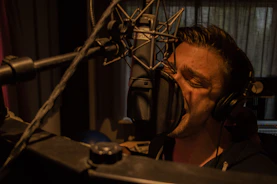 An artist wearing headphones, deeply focused while recording vocals in the booth.