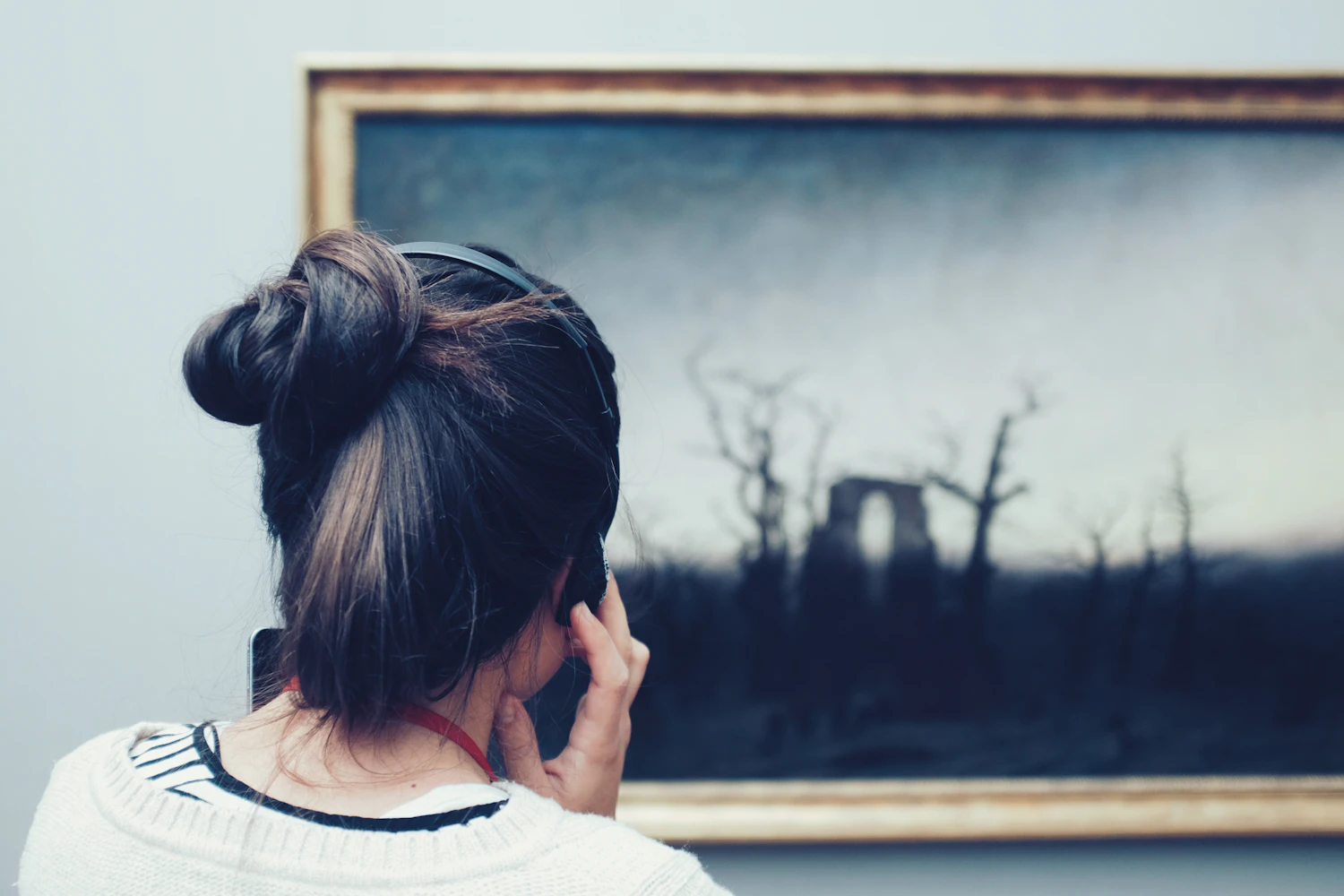 A visitor with an audio guide standing close to a dark painting