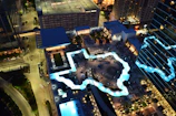 Aerial shot of a hotel rooftop pool with loungers and panoramic city views at dusk.