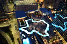Aerial shot of a hotel rooftop pool with loungers and panoramic city views at dusk.