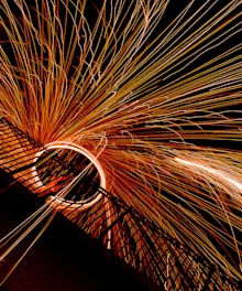 A dynamic display of long-exposure photography captures bright sparks emanating from a central point, creating an arc of light with streaks extending outward against a dark background.