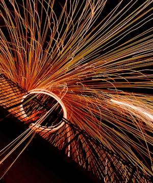 A dynamic display of long-exposure photography captures bright sparks emanating from a central point, creating an arc of light with streaks extending outward against a dark background.