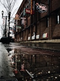 A dimly lit urban alley with rain-slicked pavement reflecting neon signs.