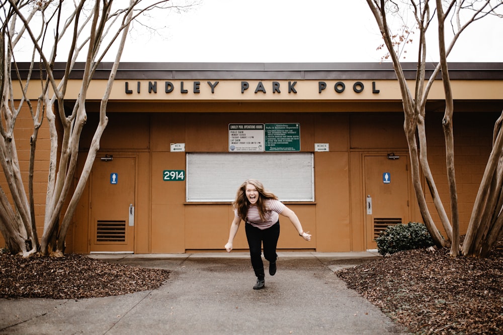 mujer riendo y corriendo frente al edificio de la piscina de Lindley Park durante el día